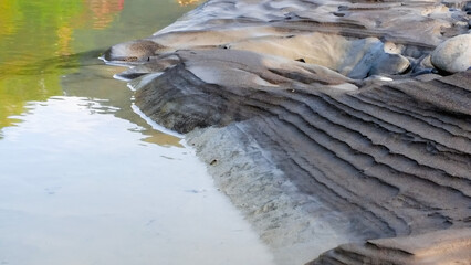 Clear green river water and layered clay riverbank in morning. Light and shadow on earth tone mud,...