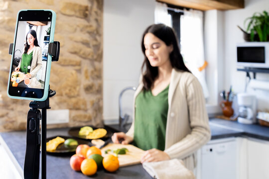 Woman recording cooking tutorial on smartphone in kitchen. Lifestyle.