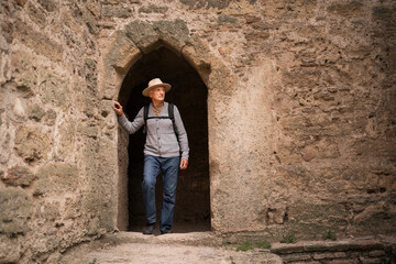 Senior man wearing hat with backpack on fortress wall arched window