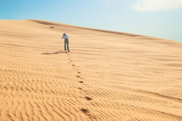Lone woman tourist walking through the vast desert, leaving footprints in the warm sand beneath a...