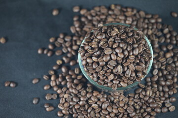 Aromatic coffee beans on dark fabric: A captivating close-up showcasing a clear glass bowl filled with rich, roasted coffee beans, spilling onto a textured dark surface.