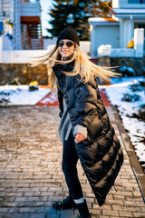 Snowy day for a young woman!. A young woman wearing a black puffer coat and beanie spins joyfully...