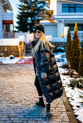 Woman in coat on snowy path. A woman strolls down a snowy walkway wearing a long black coat and hat, enjoying a sunny winter day.