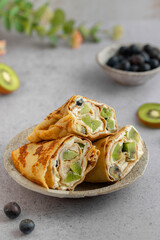 Crepe roll cake with cream cheese and Kiwifruit kiwi and blueberries. Crêpes or thin pancakes with fruits. Sweet Breakfast or Brunch. Maslenitsa, Mardi grass traditional meal.