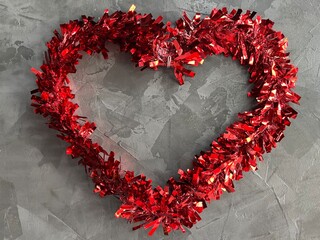 A festive red tinsel heart decoration on a gray background, perfect for Valentine's Day or romantic events.