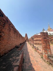 A long stone pathway flanked by ancient brick walls under a clear blue sky, leading towards a distant ornate structure.