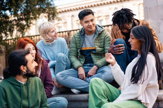 A diverse group of young friends chatting and laughing outdoors in the city. A happy multi-ethnic group of college students socializing and bonding, a concept of community and youth lifestyle.