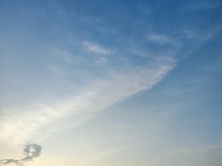 The image captures a serene sky filled with soft blue clouds, gently drifting across the horizon....