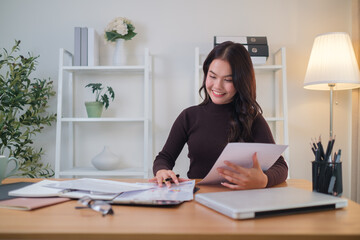 Beautiful young businesswoman holding financial reports and using laptop at her office.