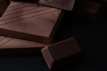 Close-up shot of a smooth chocolate bar and assorted pieces against a dark background, emphasizing texture and richness.
