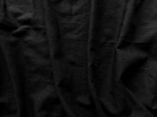 Wrinkled black fabric texture background with wavy fabric surface. The black fabric texture is soft and smooth with a clean and minimalist style. Abstract soft dark black fabric wavy smooth elegant.