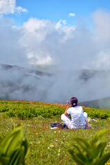 Young girl sitting on mountain grass and looking at clouds
