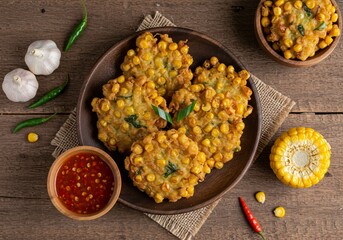 Crispy Indonesian corn fritters, known as bakwan jagung, served on a rustic plate with spicy chili sauce, fresh garlic, and red and green chilies on a wooden table.