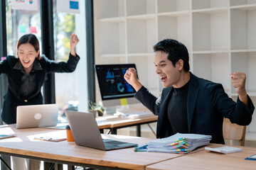 Excited business team celebrating success looking at laptop in office