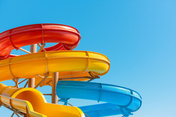 A bright and colorful set of twisting water slides in red, yellow, and blue against a clear blue sky, part of an outdoor water park attraction.