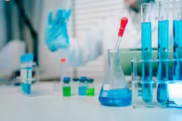 Lab table with a blue beaker and a red dropper. The table is cluttered with various glassware and...