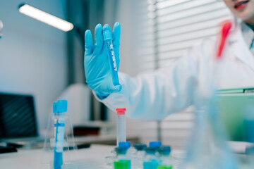 Scientist is holding a blue tube in a lab. The tube is labeled with the word "test." The scientist is wearing a lab coat and gloves.