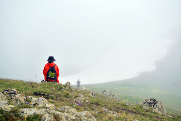 Young girl in red jacket sits on stone in foggy mountains