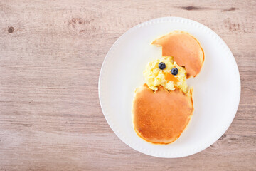 Fun Easter breakfast. Hatching scrambled egg chick and pancake egg. Top down view on a wooden background.