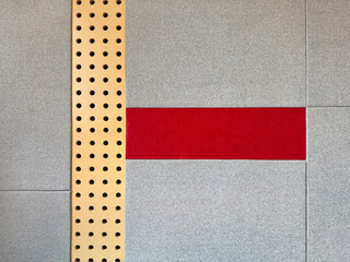Series of grey upholstered panel wall with red fabric and perforated gold metal plate. This...