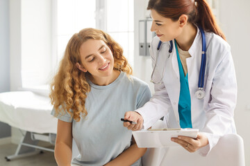 Female friendly doctor talking with a happy smiling young woman patient sitting in office and...