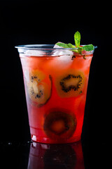 cold lemonade with kiwi, strawberries and mint in a plastic cup to take away on a black background