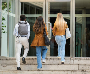 Back view of multiethnic college students walking up the stairs and entering university building