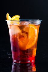 cold lemonade with orange and cherry in a plastic cup to take away on a black background