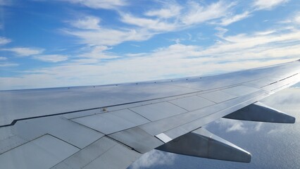 Airplane wing gliding over Gran Canaria, revealing the sparkling ocean and fluffy clouds beneath a...