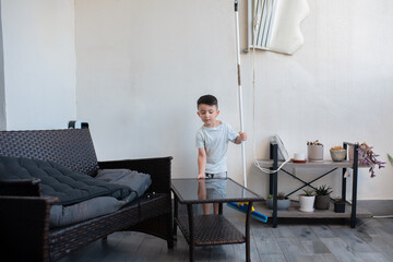 Boy washing floor with mopping stick in balcony of modern apartment. Happy child cleaning at home...
