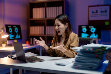 Stressed Asian businesswoman yelling at laptop in office at night