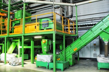 Industrial recycling plant with green machinery. Waste sorting facility with conveyor belts. Recycling process in factory setting. Large-scale recycling equipment in workshop.Waste material processing