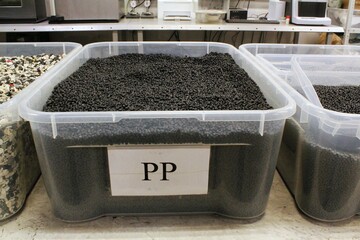 Plastic pellets in transparent storage containers. Black plastic granules in clear bins....