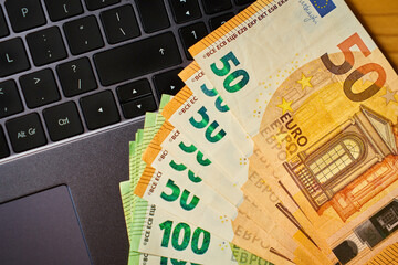 Euro banknotes on laptop keyboard. Concept of cash money, digital payments and financial...