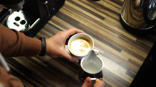 Bartender adds milk to the coffee from the milk jug and draws a heart on it. High quality 4k footage