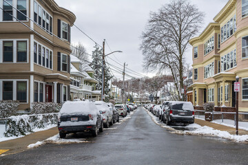 Snow-covered residential street with parked cars and houses in Brighton, Massachusetts, USA
