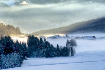 Mountain valley village shrouded in mist at sunset in winter. Thick mist envelops the valley at dusk. South Tyrol, Trentino Alto Adige, Alps, Italy, Europe.