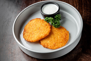 Crispy golden-brown potato pancakes served on a white plate with a small bowl of creamy dipping...