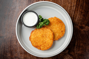 Crispy golden-brown potato pancakes served on a white plate with a small bowl of creamy dipping sauce and fresh parsley garnish.