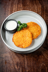 Crispy golden-brown potato pancakes served on a white plate with a small bowl of creamy dipping sauce and fresh parsley garnish.