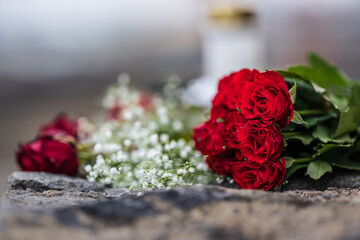 bouquet of red roses resting on a stone with a candle in the background.