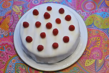 Eine Fondant Torte mit Himbeeren drauf auf einer Tortenplatte mit goldenem Rand. Die Platte steht...
