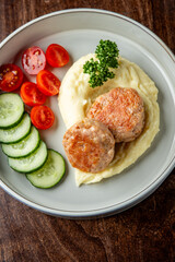 A delicious plate of meatballs served with creamy mashed potatoes and a fresh side of cucumber slices and cherry tomatoes, garnished with parsley.