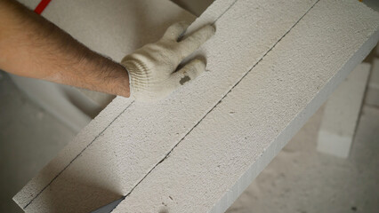 Closeup. Builder sawing aerated concrete block with hand saw at construction site. construction, Building manual work. Construction worker in gloves sawing aerated concrete block