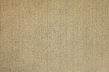 Texture and background of yellowed shade. The building wall, painted with beige water-based paint. Old surface in faded beige color with stains and strokes. The striped backdrop with streaks and drips