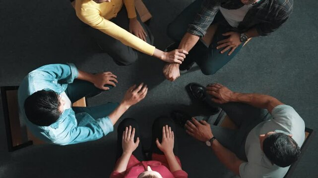 Top down aerial view of diverse business people hold wrist while sitting circle together. Faithful prayers holding wrist or hand of each other. Represented teamwork, unity, togetherness. Symposium.