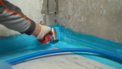 Construction worker applying waterproofing material with brush in corner of bathroom
