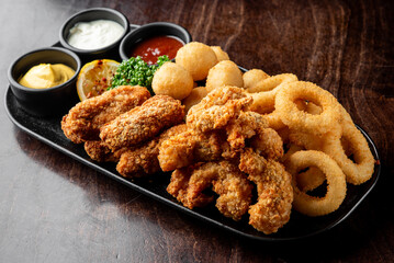 A delicious platter of crispy fried chicken wings, onion rings, and golden mash balls, accompanied...