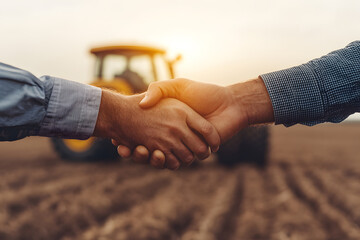 Agricultural Partnership: Farmers shaking hands on a plowed field with a tractor in the background, symbolizing trust and cooperation in farming ventures.