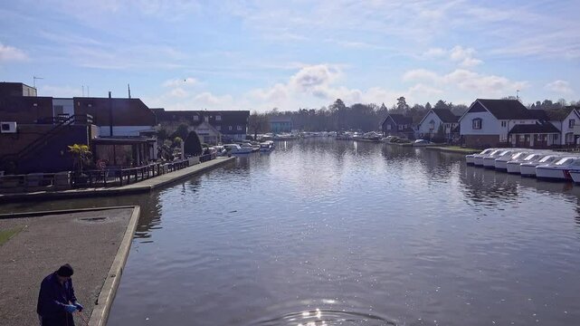 View down the River Bure with a man magnetic fishing in the village of Wroxham, Norfolk Broads. As captured from the bridge on a sunny morning in the springtime